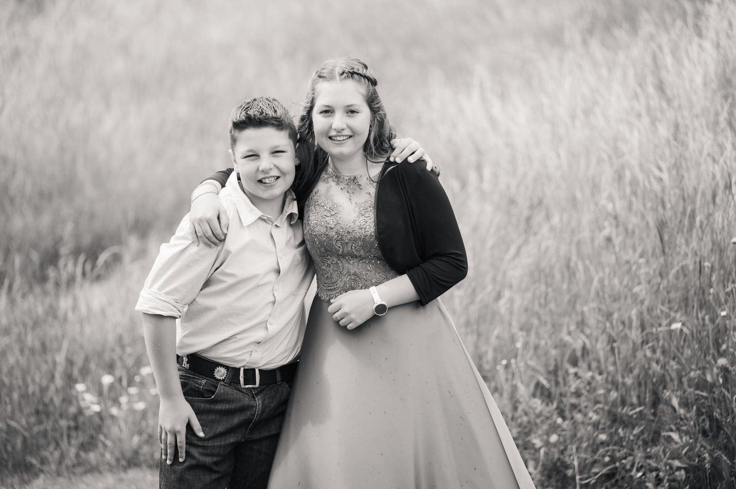 Black and white photo of a young boy and teenage girl smiling together in a field, dressed in formal attire.