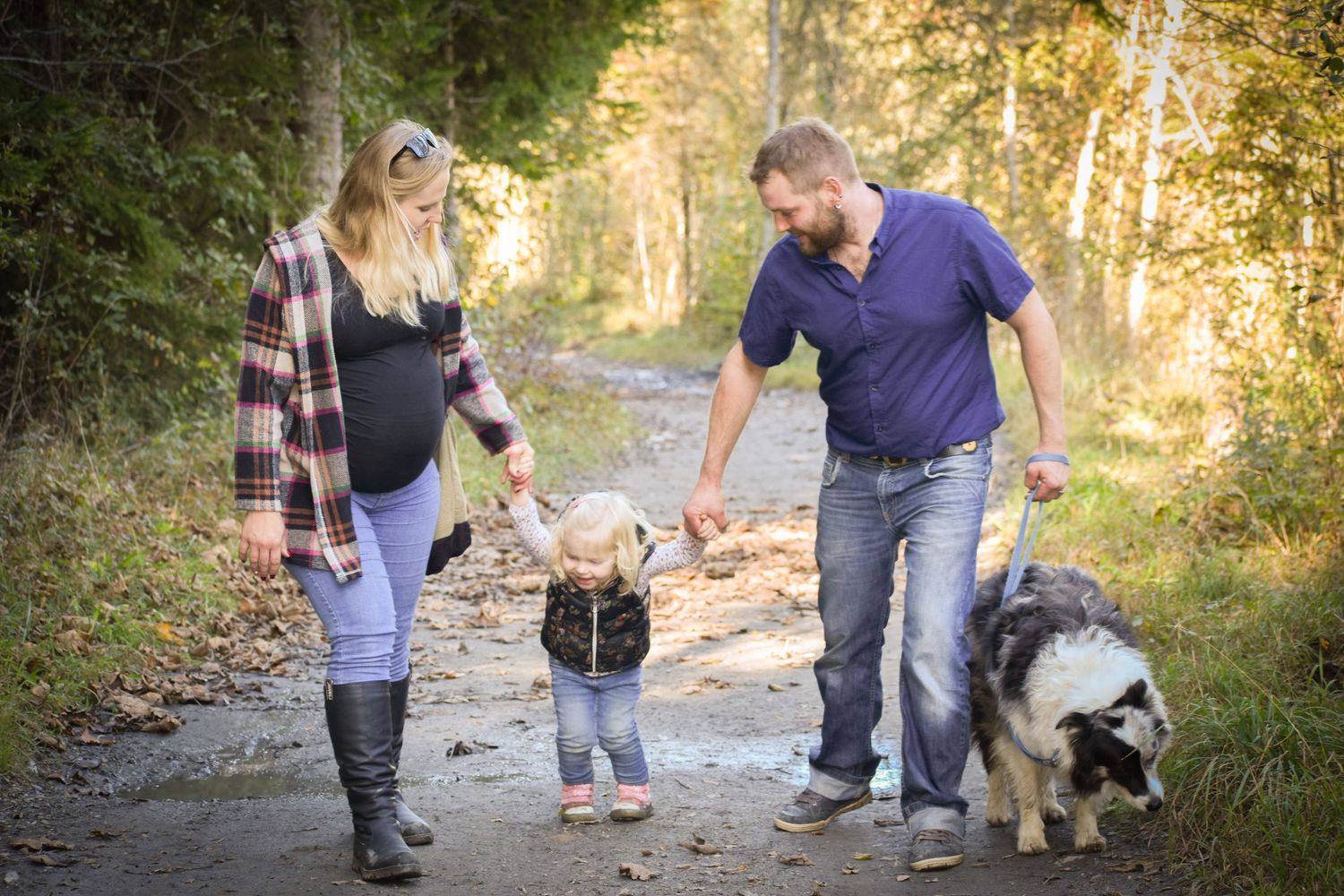 Family walking with their dog on a forest trail during an autumn afternoon.