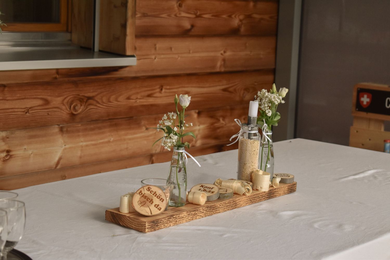 Simple table decor featuring glass vases with flowers and a wooden serving board on a white tablecloth.