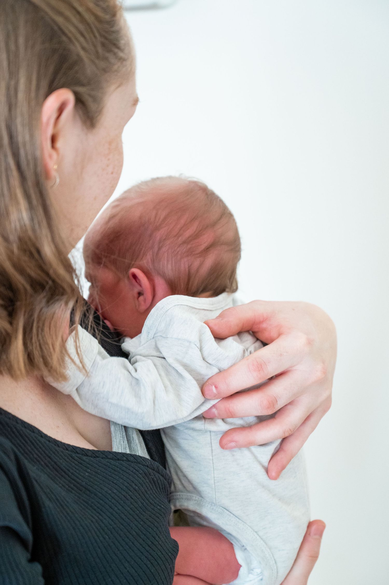 Tender moment of newborn being cradled in white onesie.