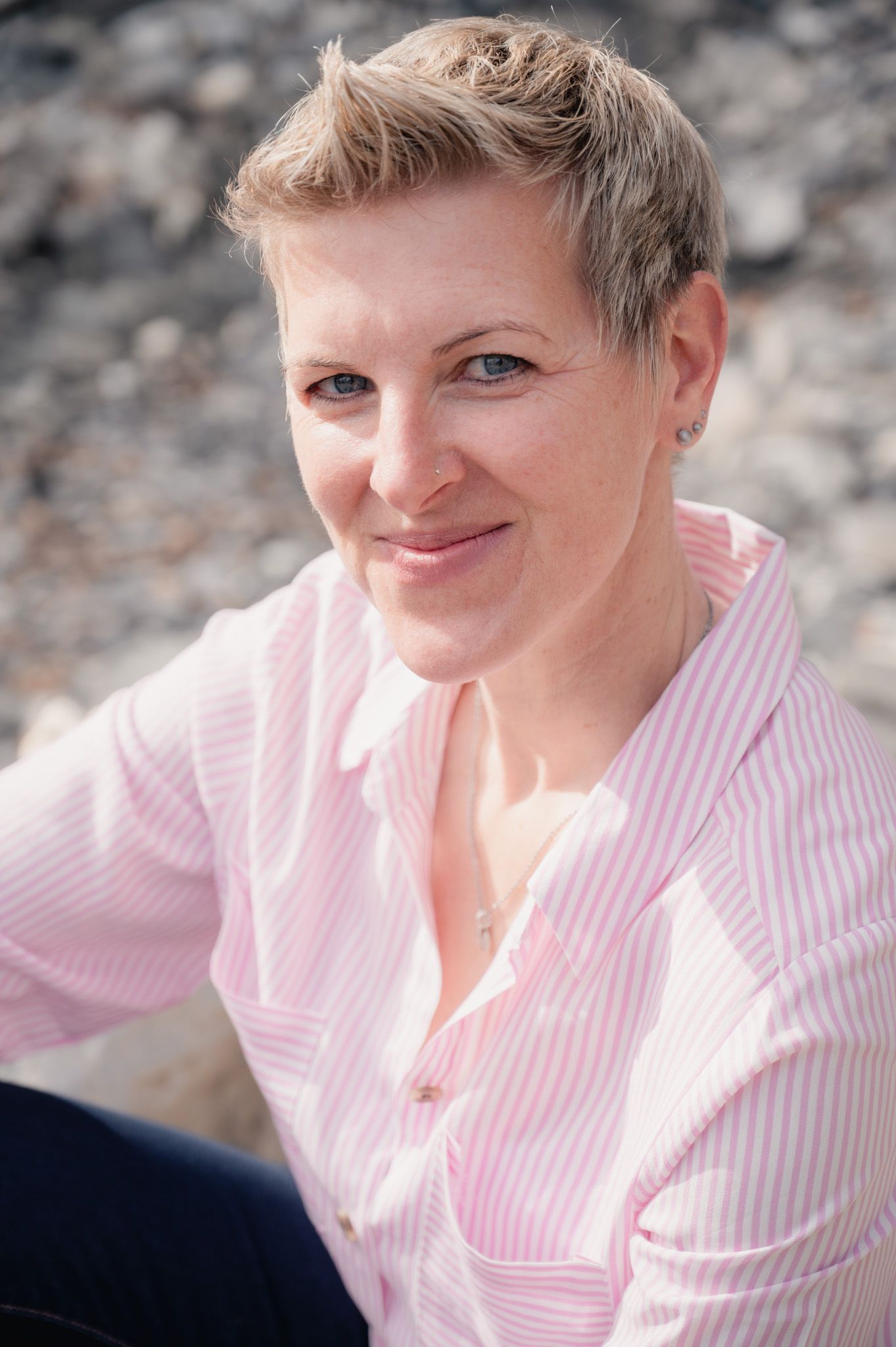 Person wearing pink and white striped blouse sitting against a stone wall background.