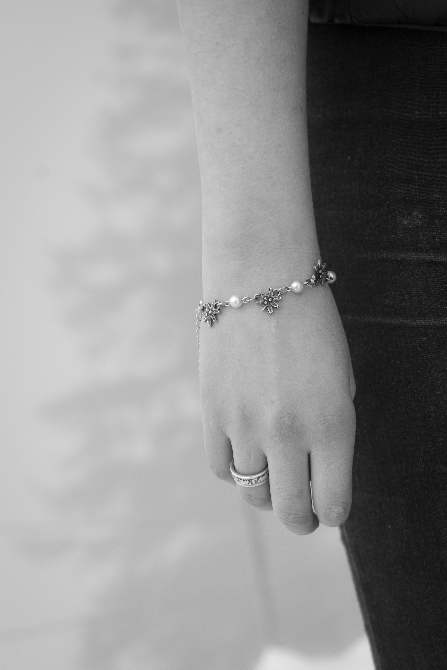 Black and white close-up of delicate jewelry and rings on hands.