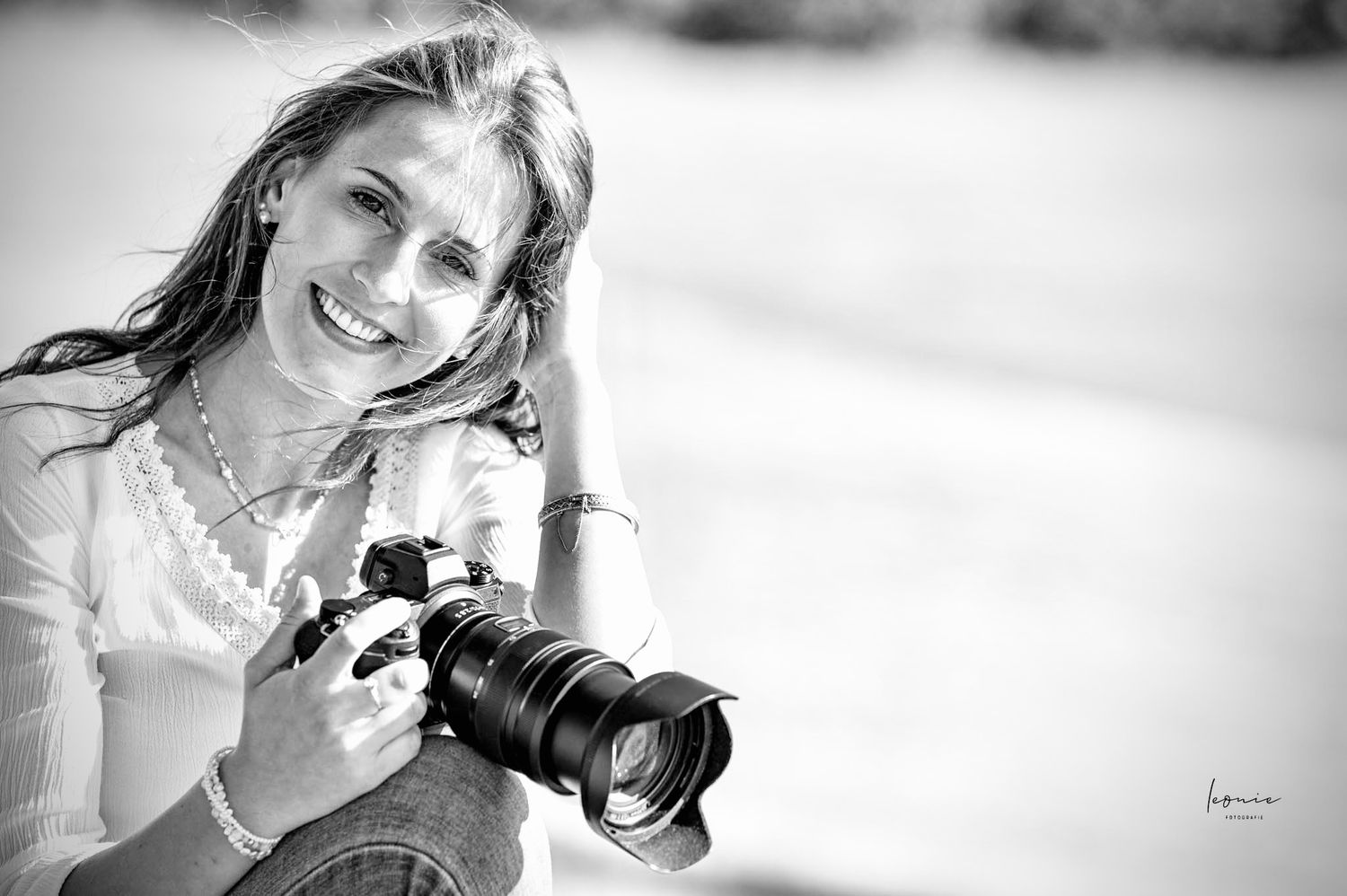 Smiling woman holding a professional DSLR camera outdoors, black and white portrait photography.