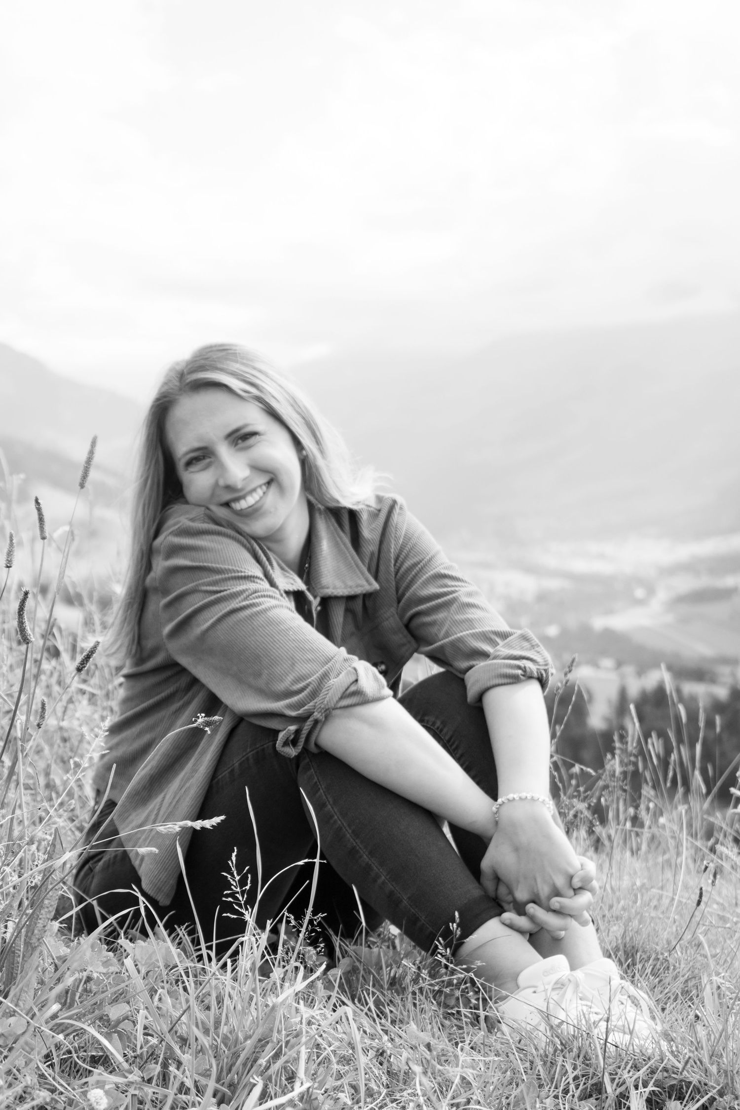 Black and white portrait of person sitting in mountain grass with scenic valley view.