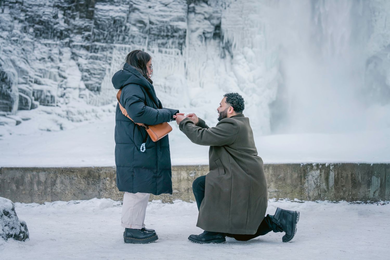 A person photographs a frozen waterfall in winter with snow and ice formations surrounding the scenic landscape.