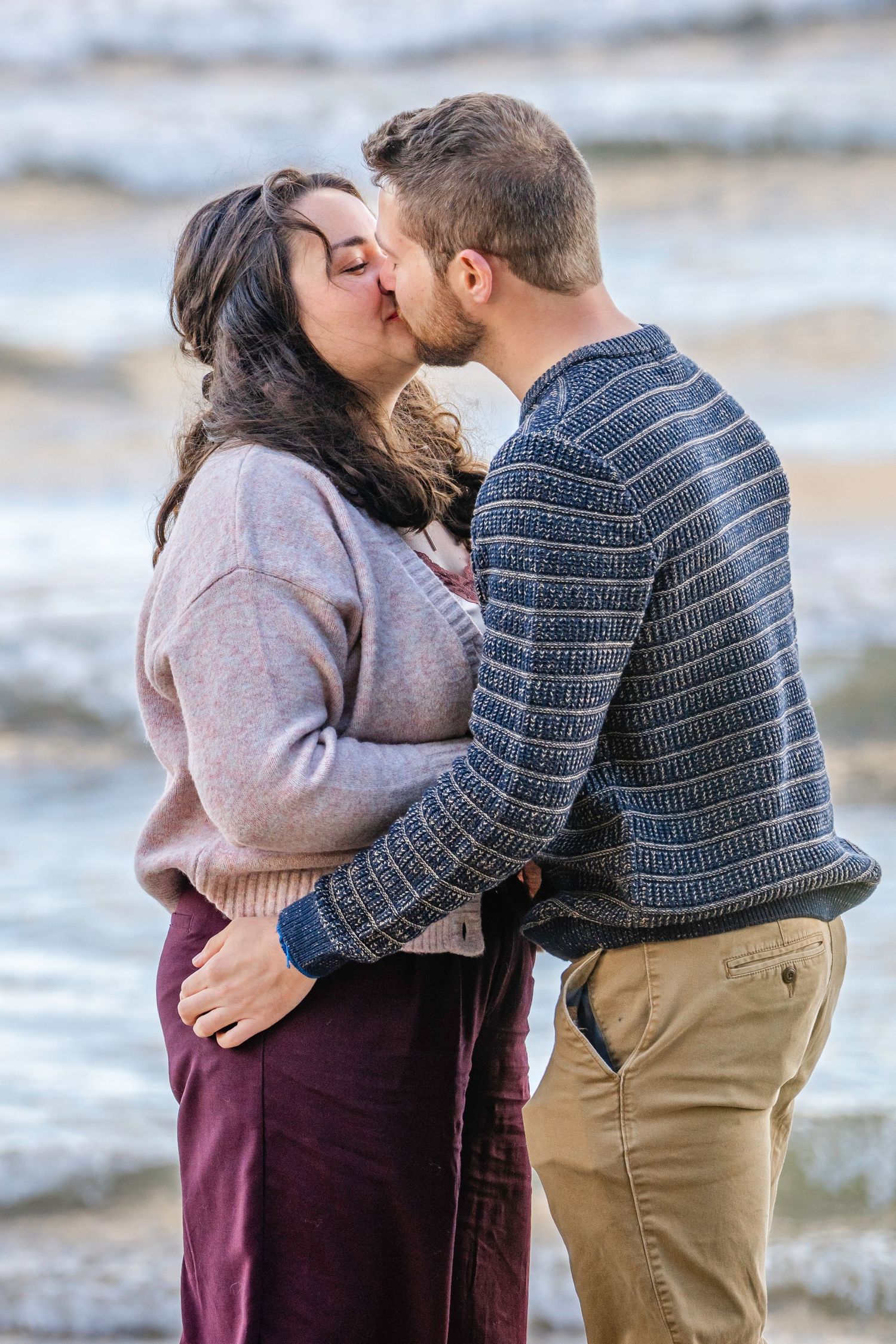 A romantic couple embraces and shares a tender kiss outdoors on a winter day.