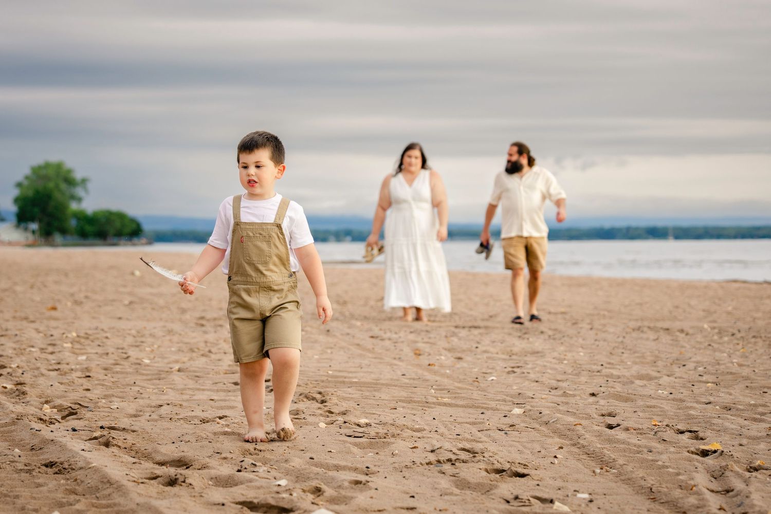 Family members walk together along a sandy beach during sunset with soft overcast lighting.