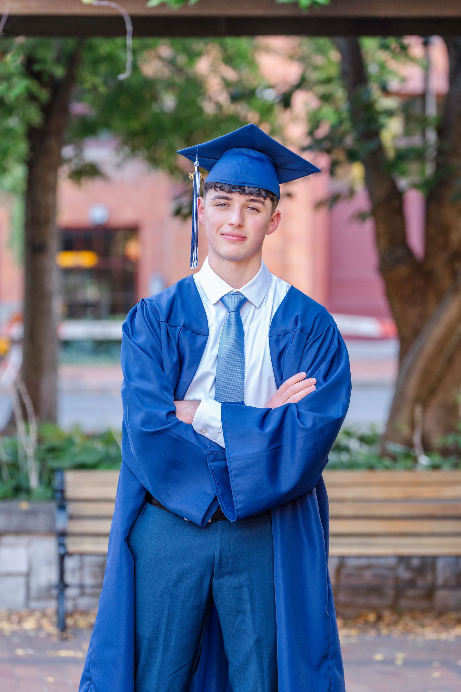 Graduate in bright blue cap and gown poses outdoors on campus during graduation photoshoot.