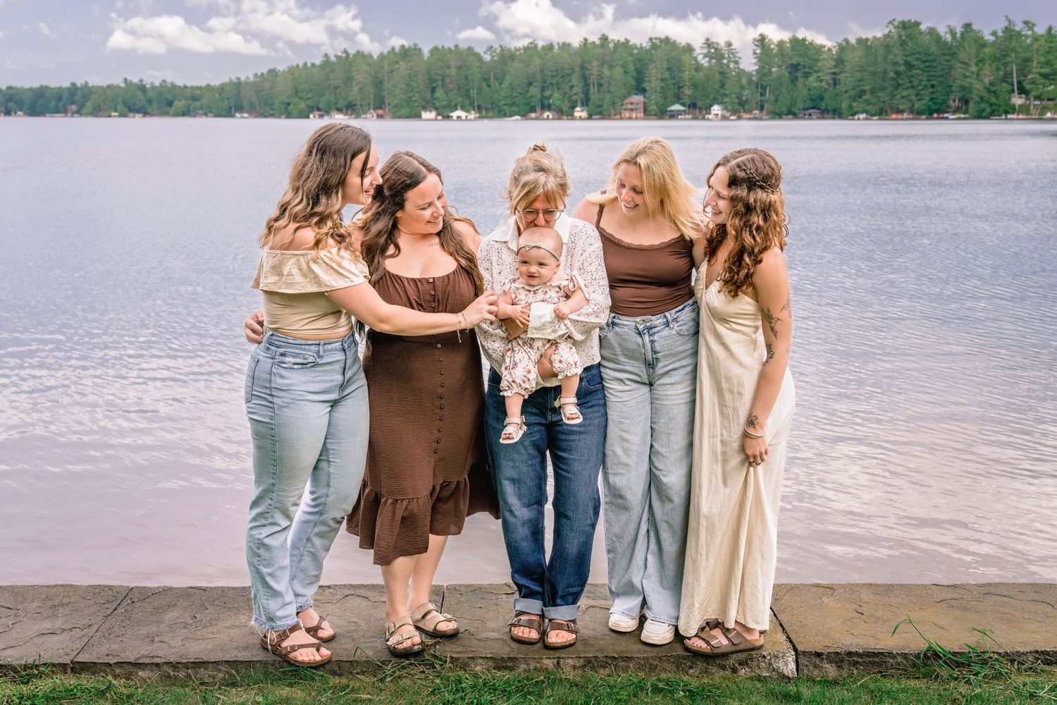 A group stands together on a lakeside path wearing coordinated neutral-toned casual outfits.