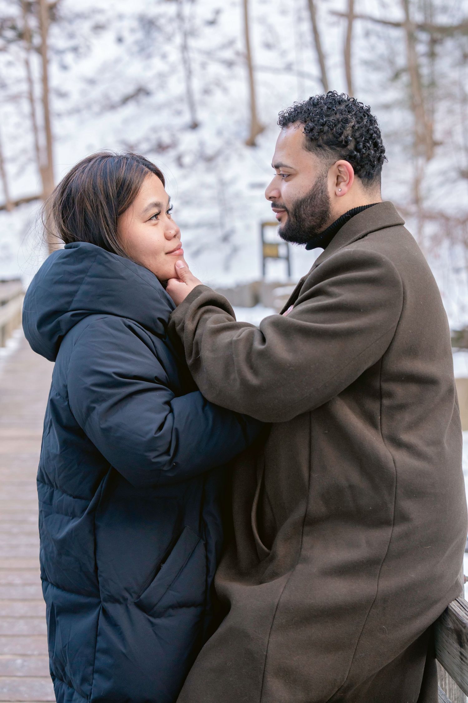 Two people share an intimate moment in a snow-covered forest setting.
