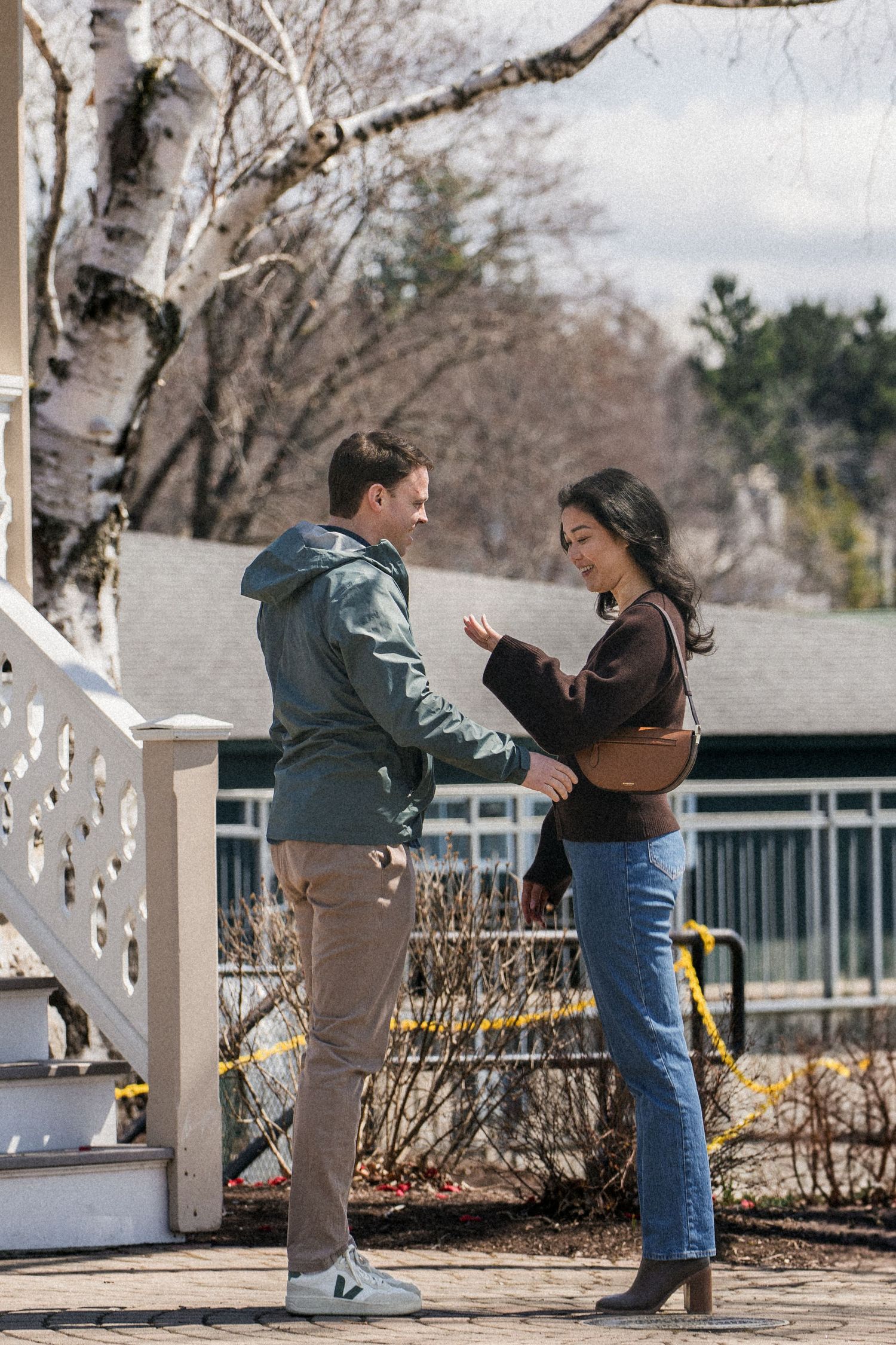 A couple dances together on an outdoor patio with white railings and bare trees in the background.