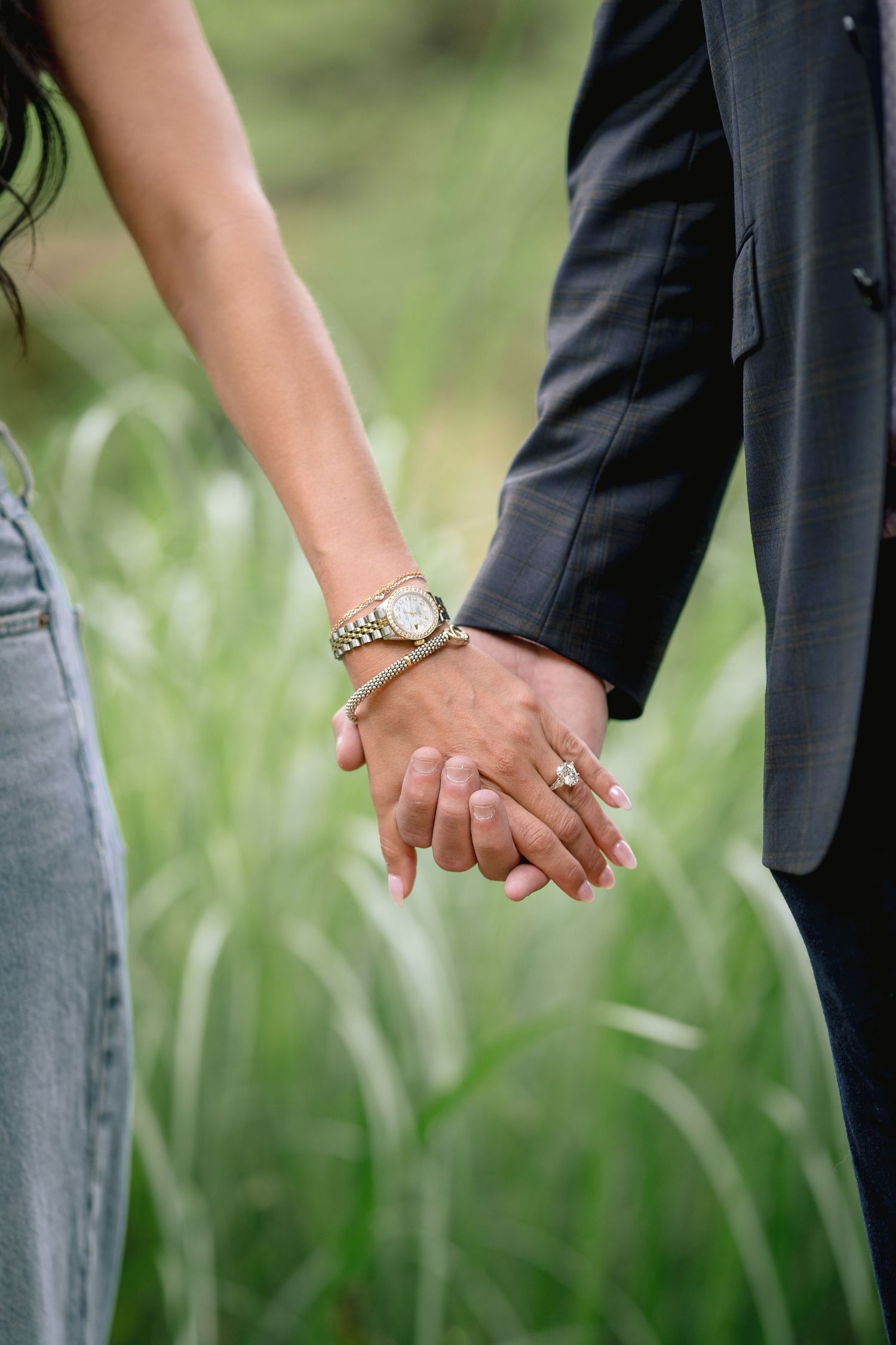 Close-up of two people holding hands outdoors with green foliage in the background.