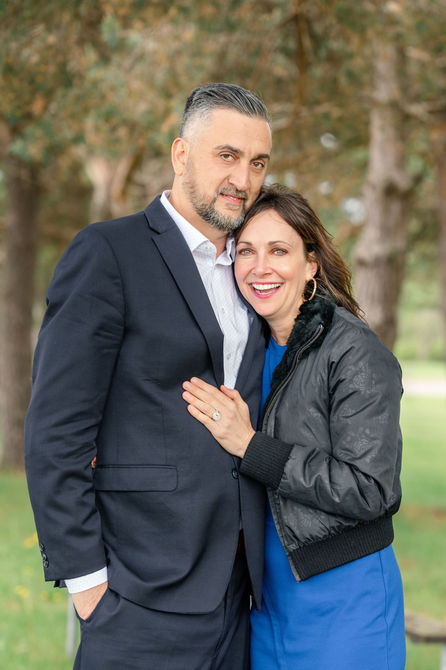 A couple shares a tender moment in a park setting with trees in the background.
