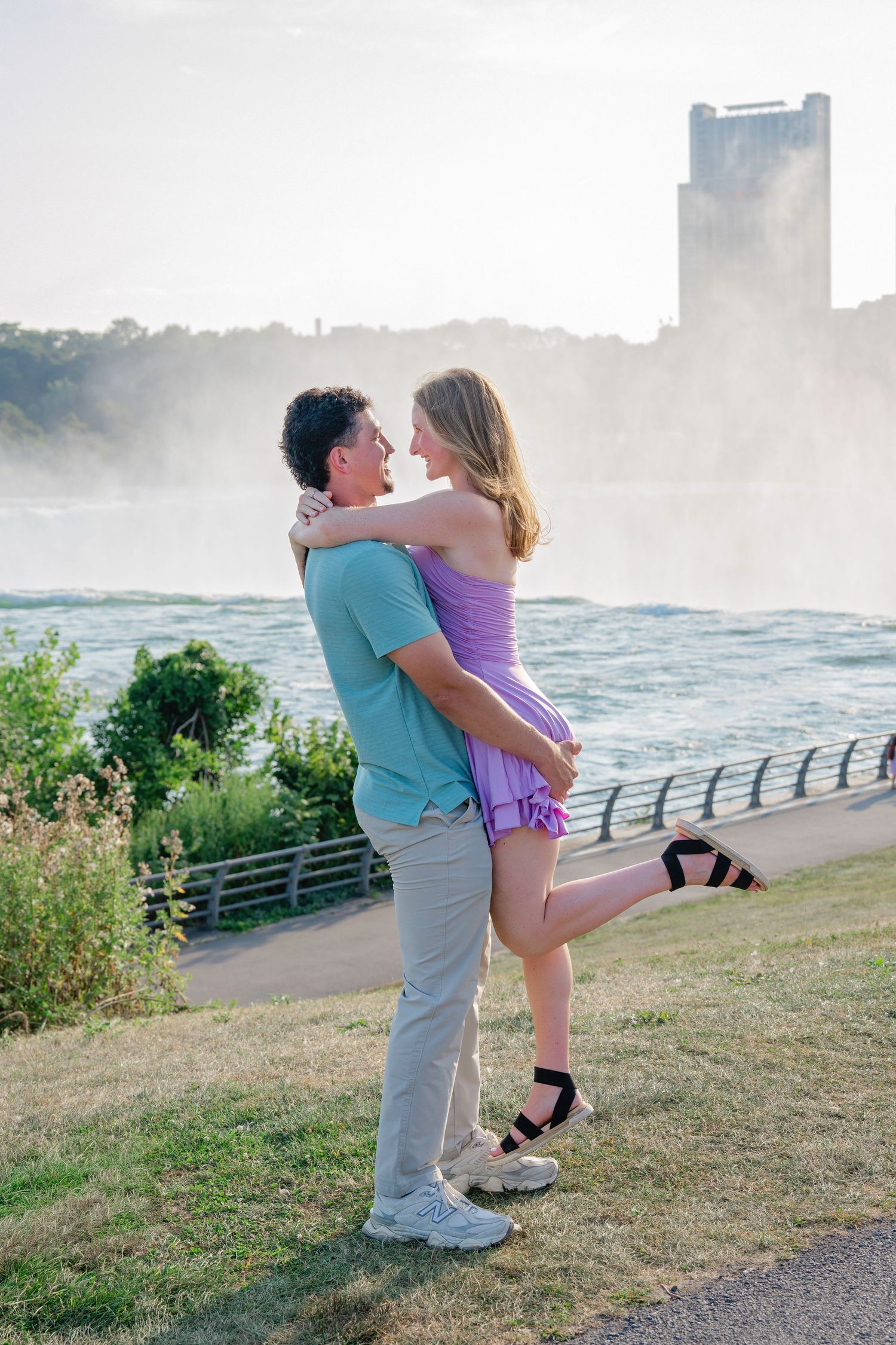 A couple embraces romantically near misty Niagara Falls during sunset.