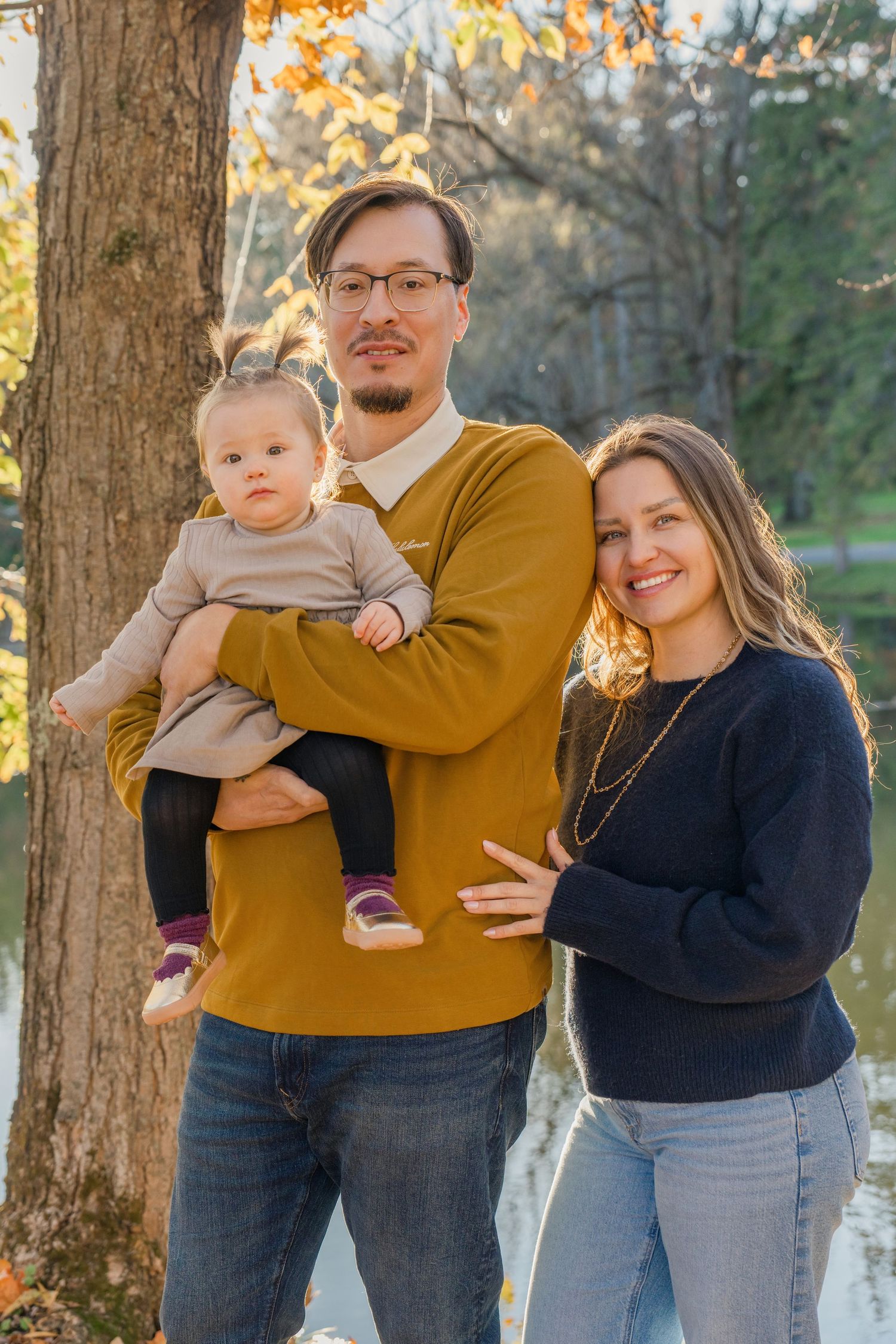Family poses together against autumn trees during golden hour photoshoot in a park.
