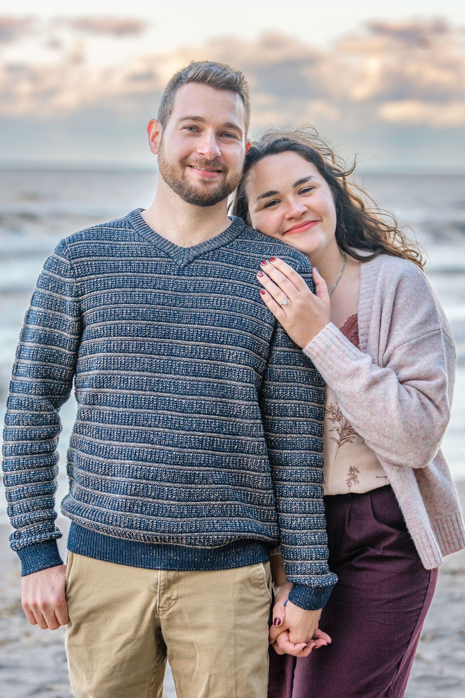 A couple shares a romantic moment together on the beach at sunset wearing coordinated sweaters. Proposal and engagement.