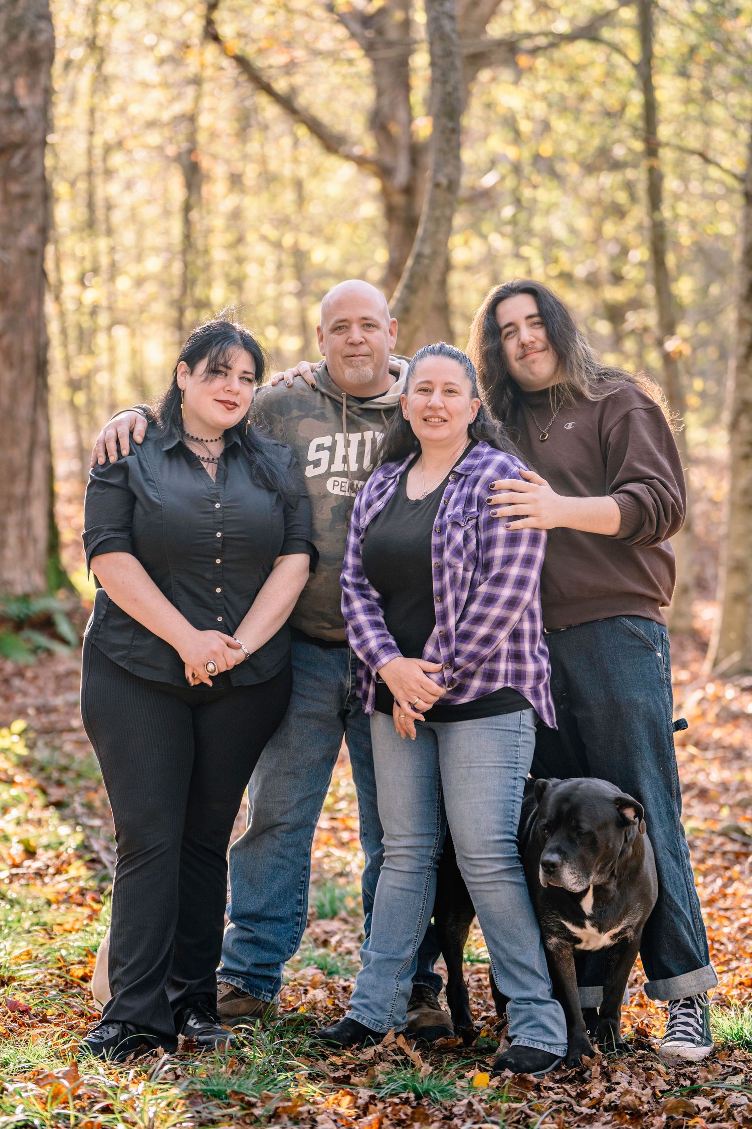 A group poses together on fallen autumn leaves in a sunlit forest setting.