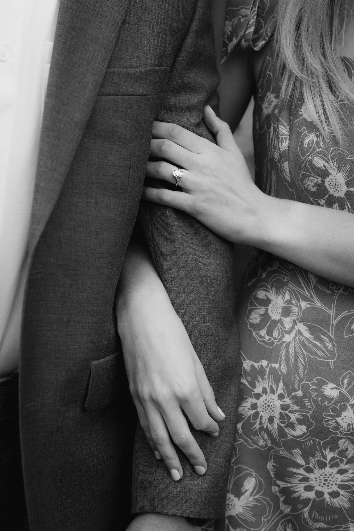 Close up of hands embracing against a dark suit jacket and floral dress fabric.