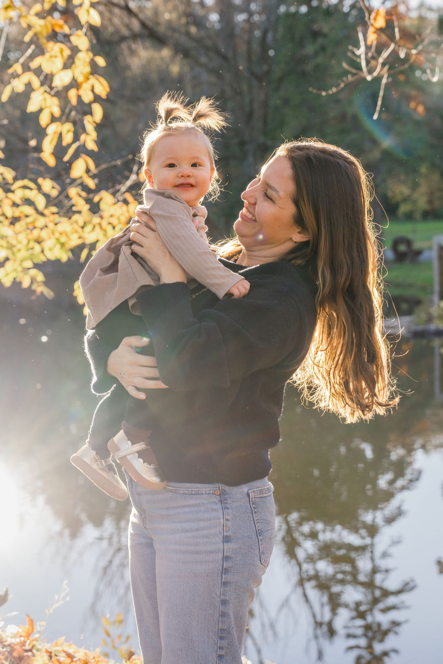 Joyful outdoor family portraits with golden sunlight filtering through autumn trees by a lake.