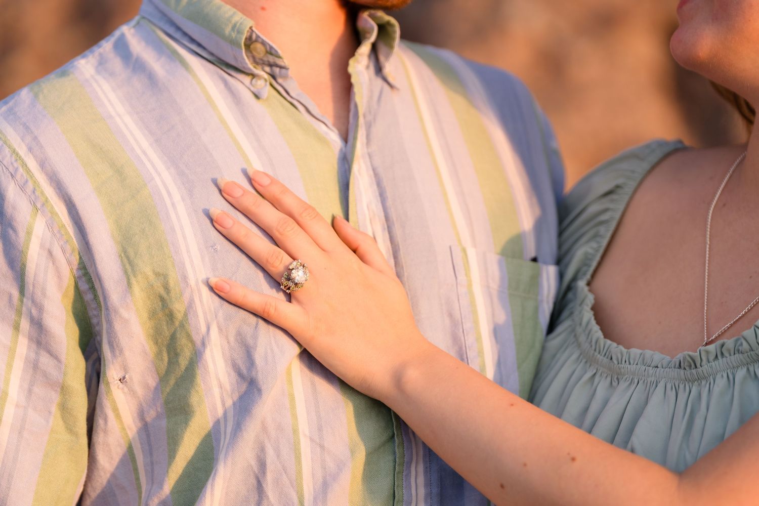 Close-up shot of an engagement ring being shown on a beach during sunset.