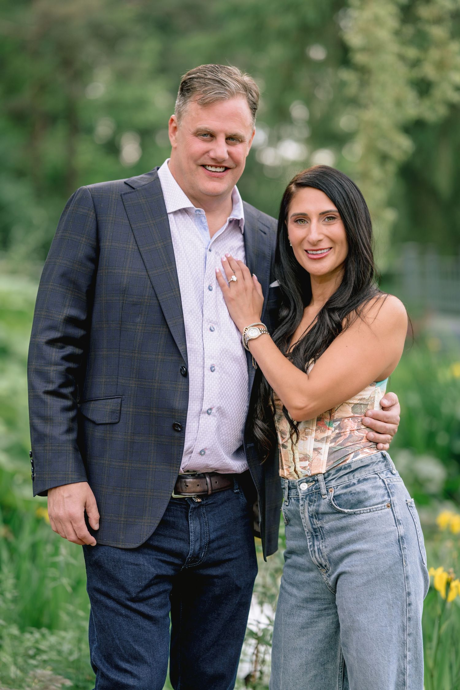 Couple posing together in a garden with yellow flowers and greenery.