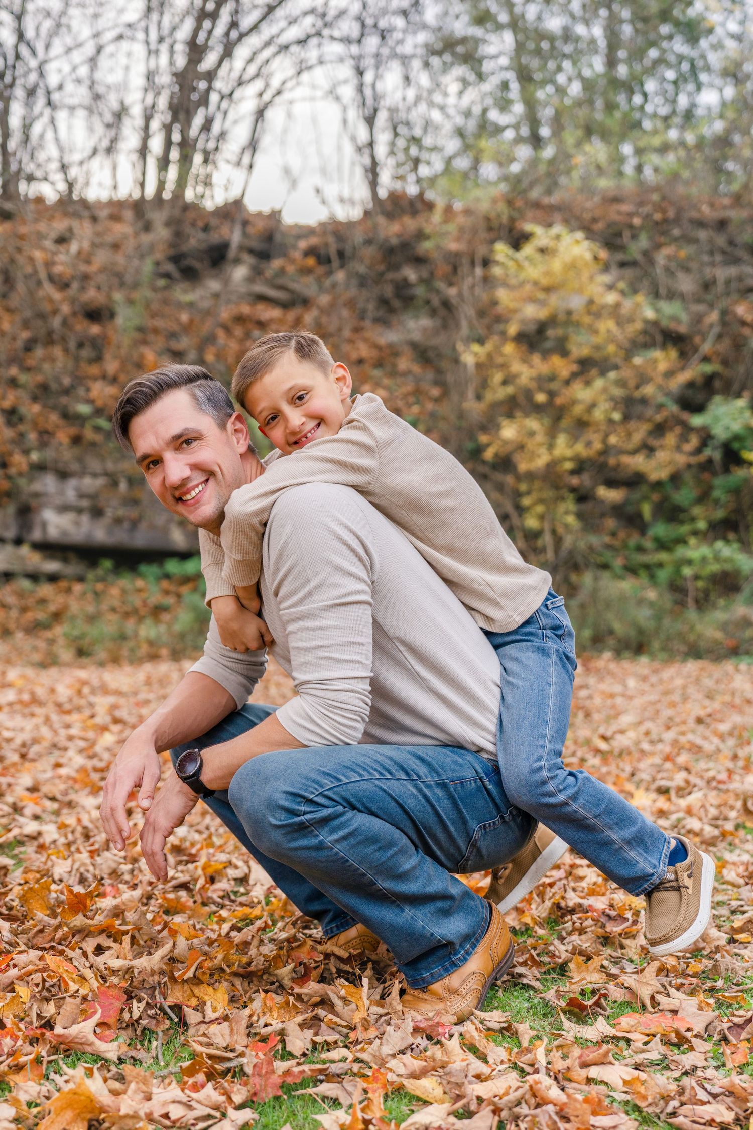 A father and child play together in fallen autumn leaves on a sunny day in the park.