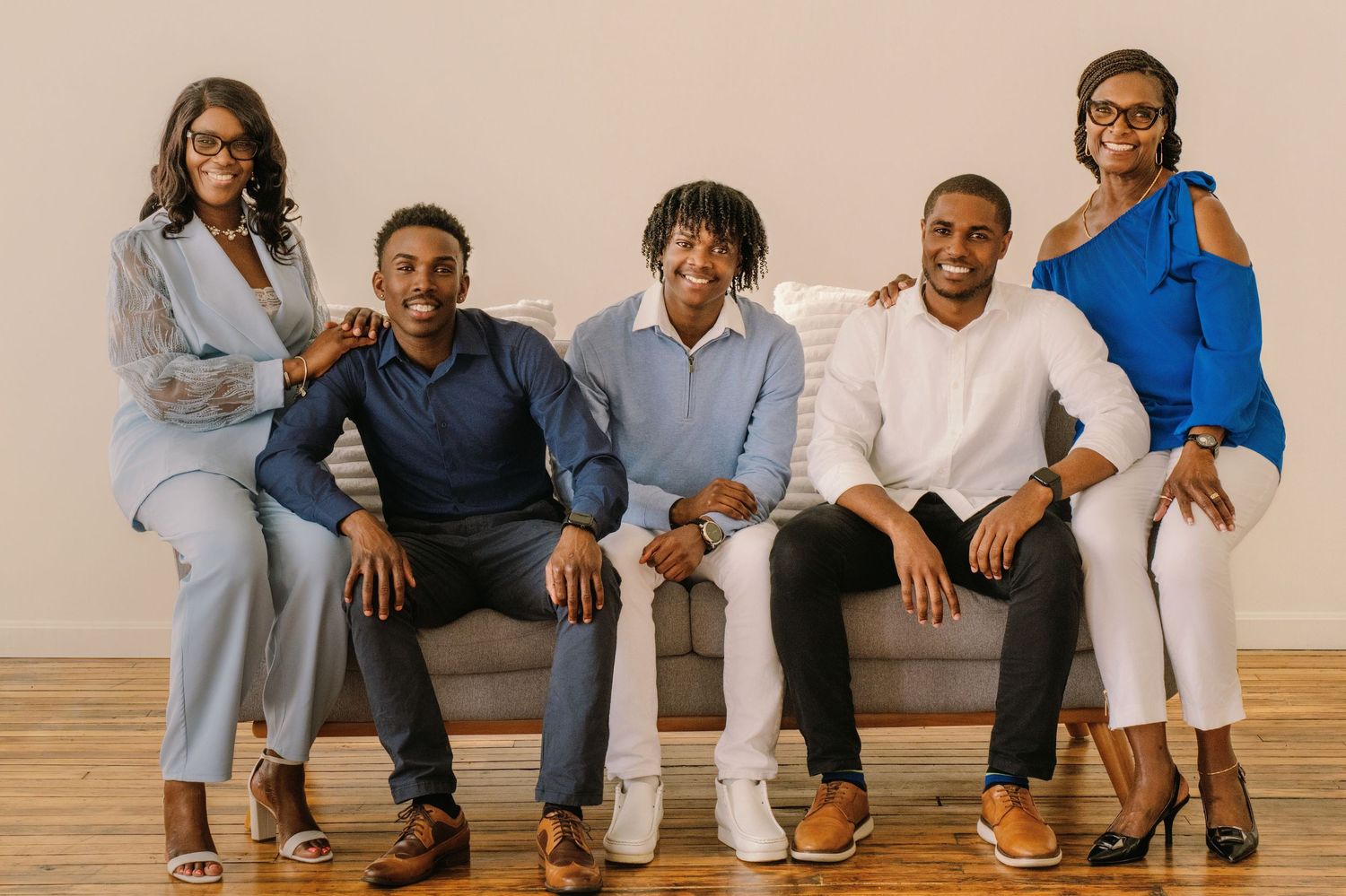 A group of people in casual clothing sit and smile together against a beige wall background.