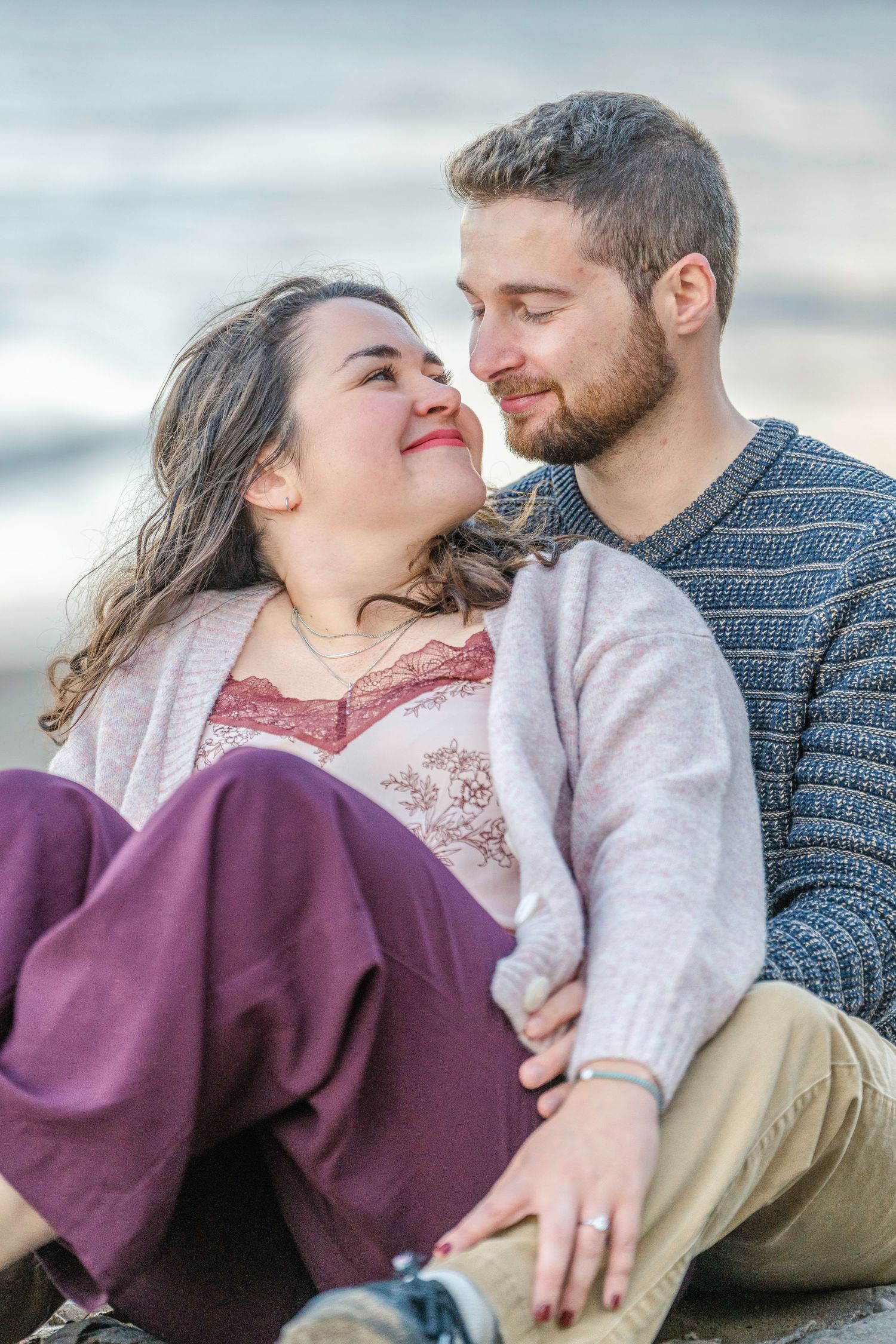 A couple embraces while sitting on the beach during a romantic photoshoot.