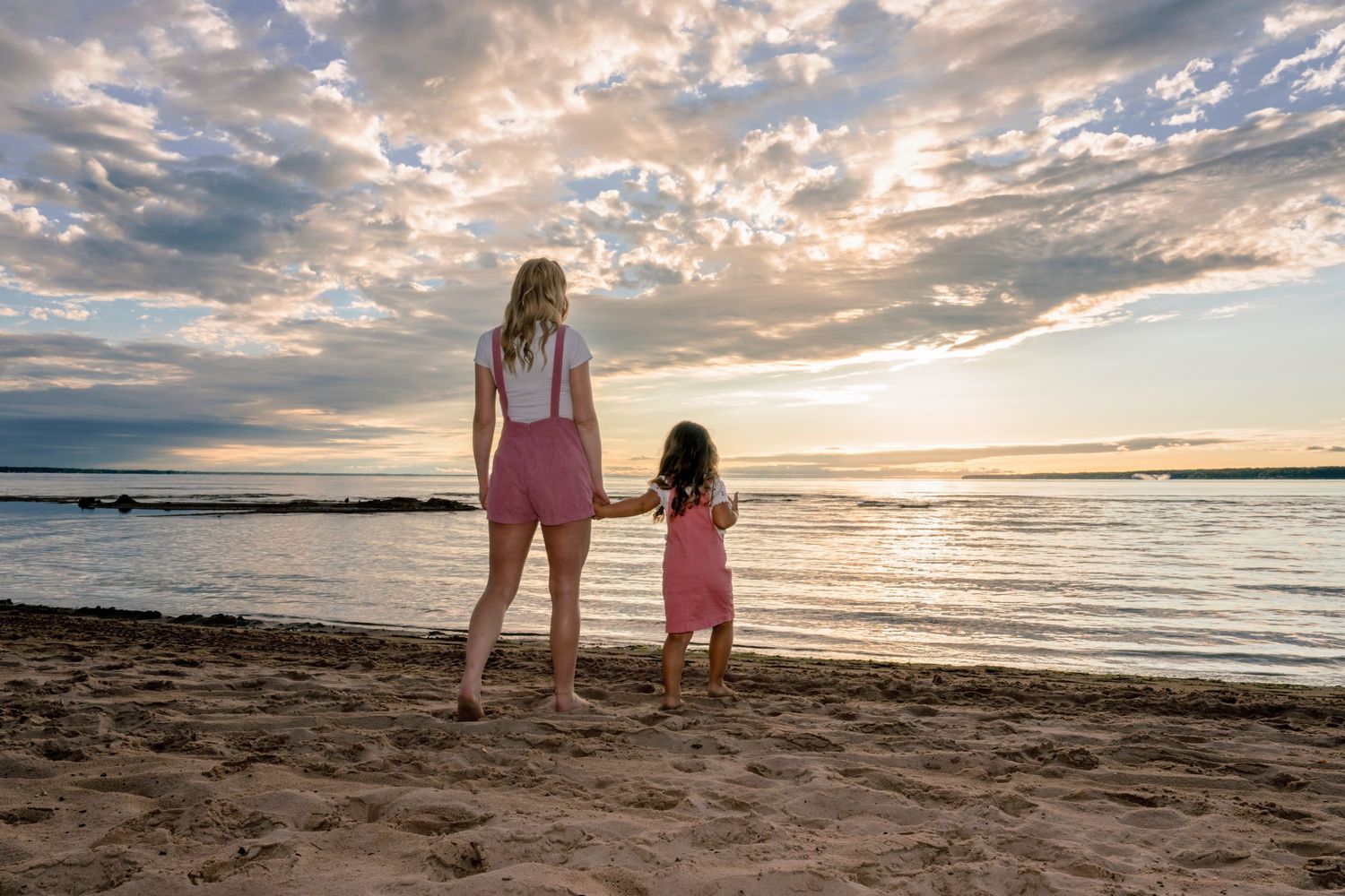 Two people standing on a beach at sunset watching the dramatic sky over the ocean.