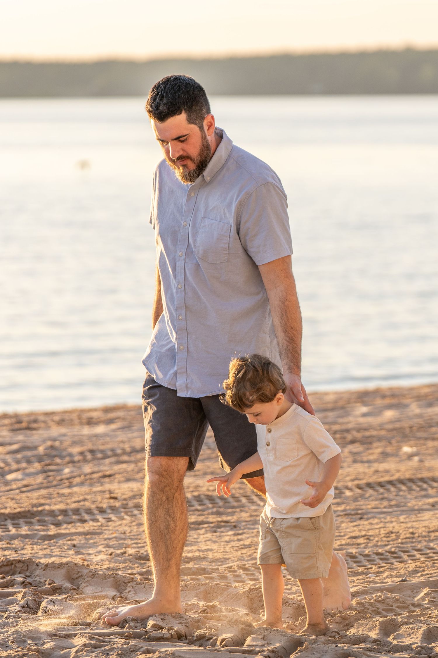 Parent and child walk together on a sandy beach at sunset creating footprints in the golden sand.