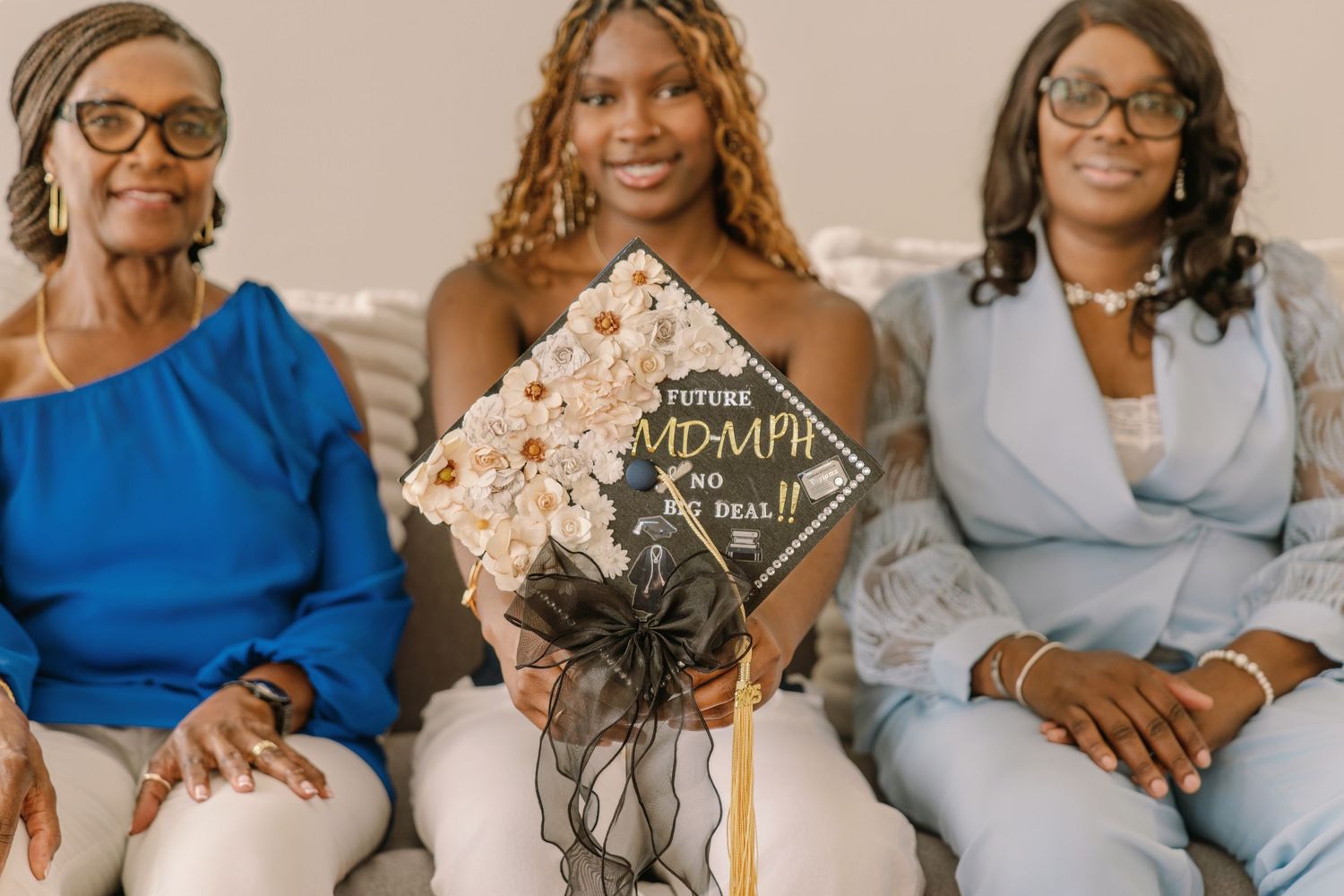 Three generations of family members sit together on a couch with a decorated graduation cap displayed in the center.