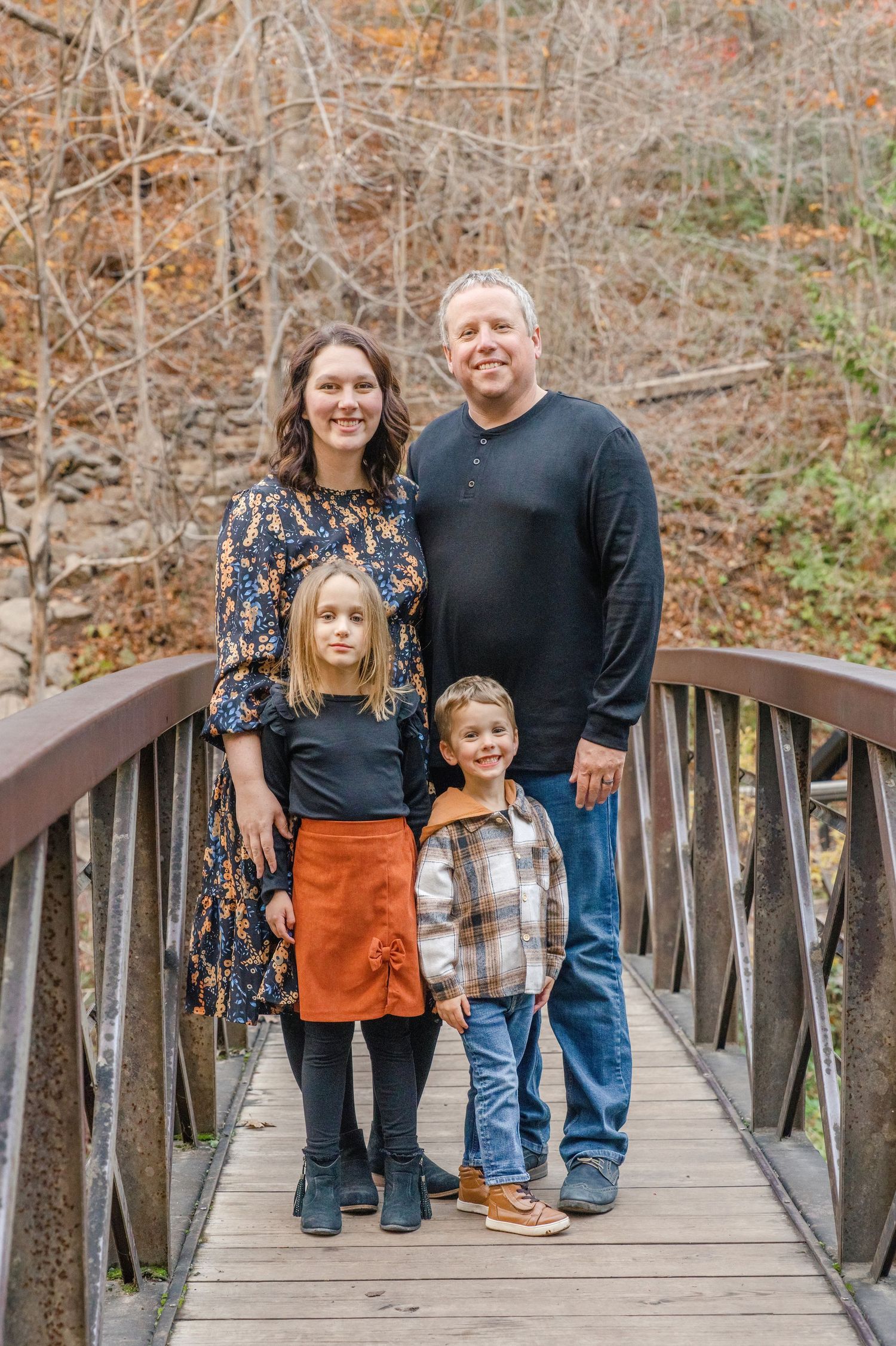 A family poses for a series of casual outdoor portraits on a wooden bridge surrounded by autumn trees.