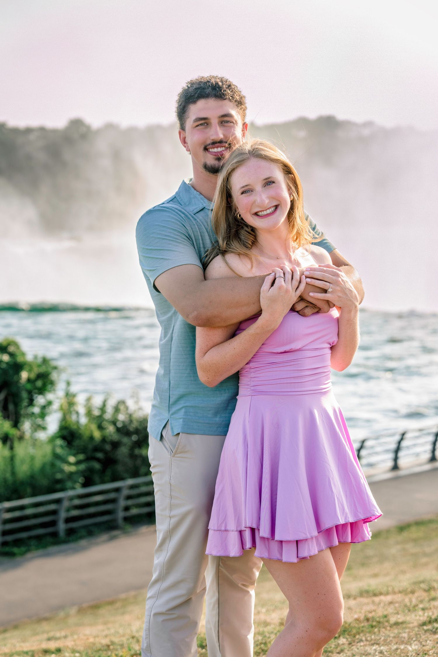 A couple shares joyful moments together near misty waterfalls at sunset.