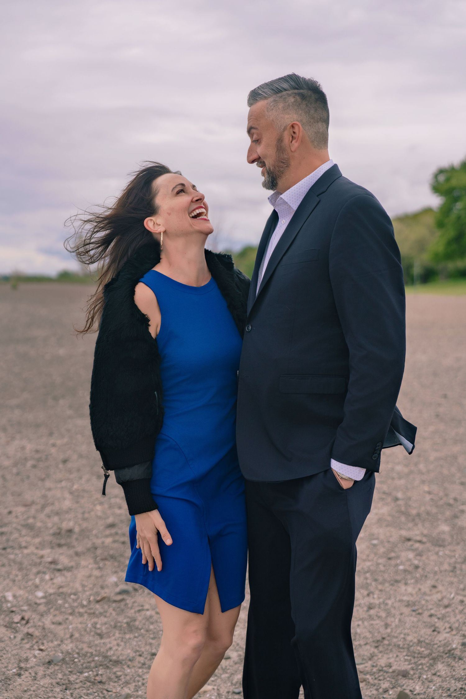 A couple shares a joyful moment together in an outdoor field, with one wearing blue and the other in black attire.