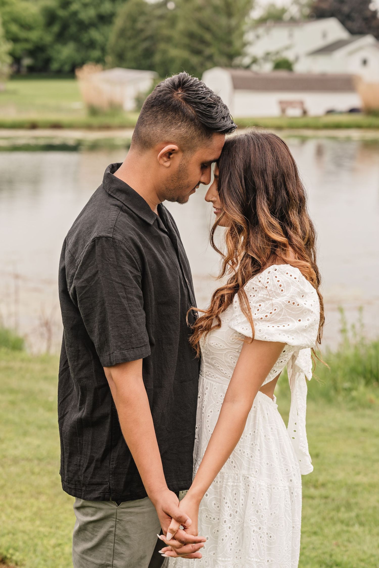 A tender moment between a couple in black and white attire by a lake.