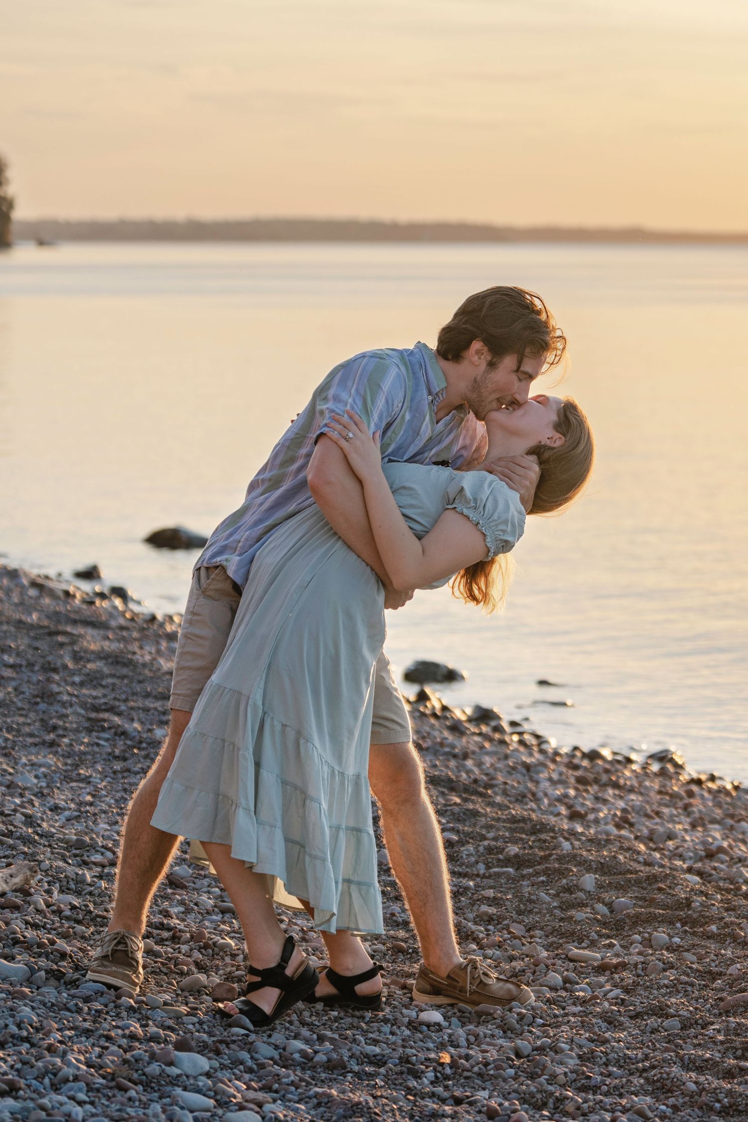 A romantic couple shares an intimate dance pose on a rocky beach during golden hour.