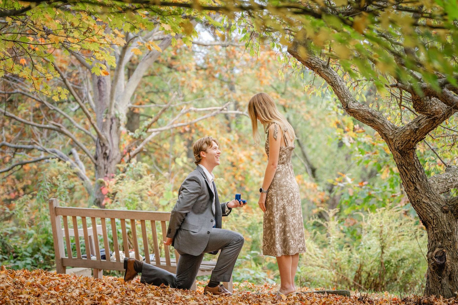A couple shares a romantic autumn moment under colorful fall foliage in a park setting.