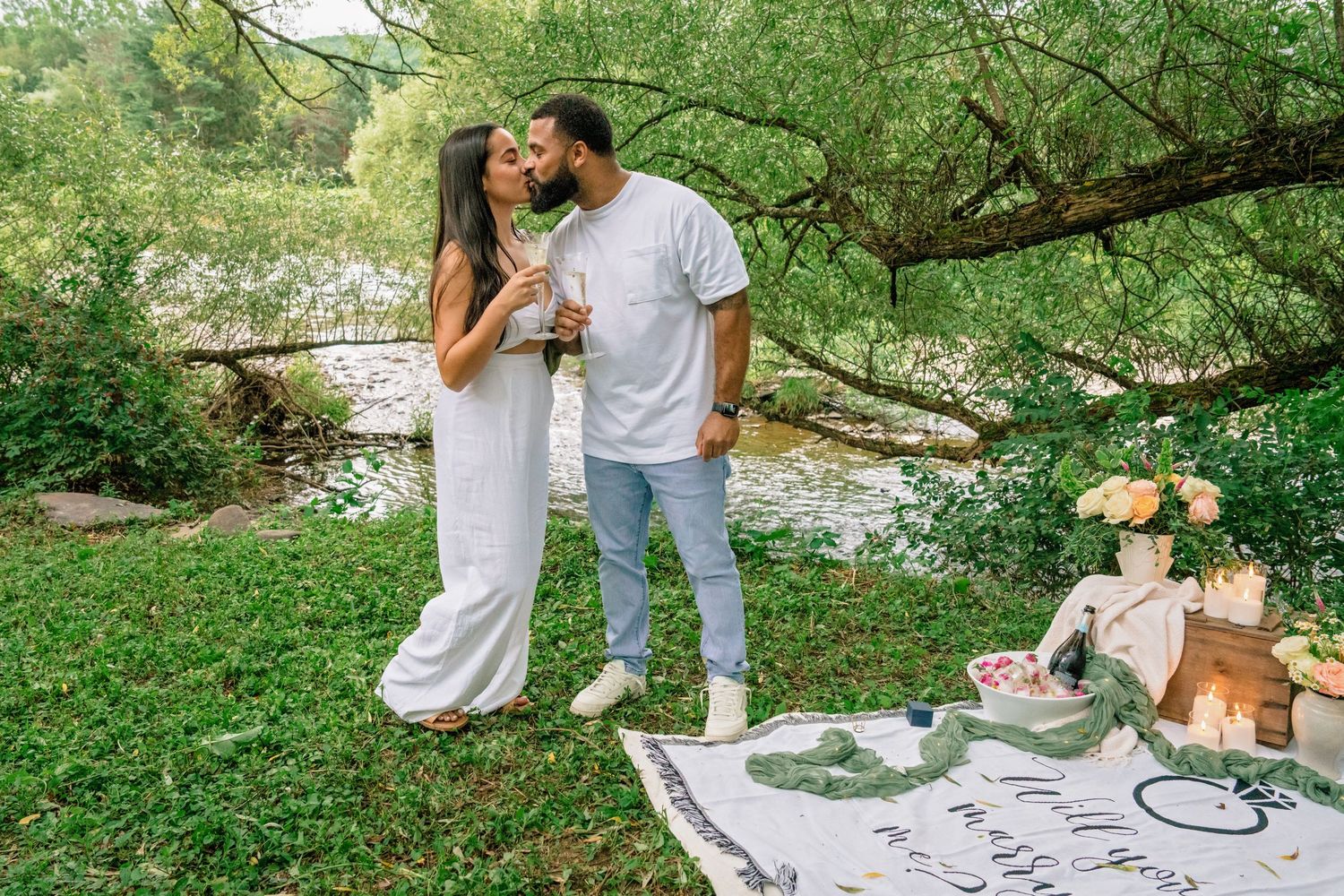 Couple enjoying an intimate forest picnic with their dog on a white blanket surrounded by greenery.