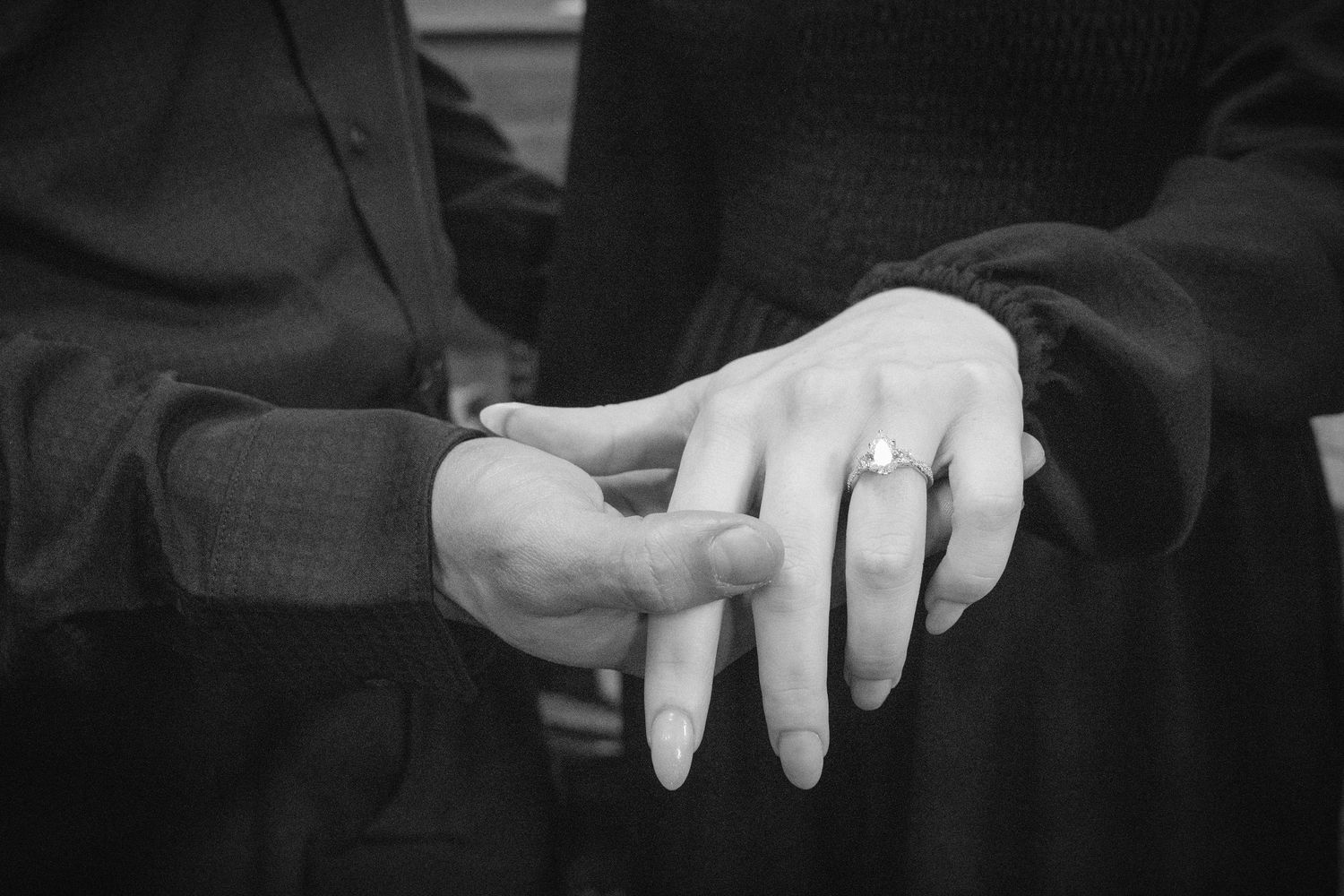Black and white photo of a couple holding hands showing an engagement ring during a marriage proposal.