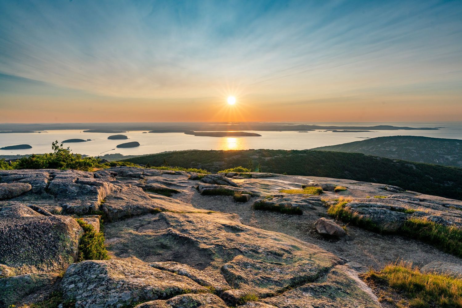 Panoramic sunset view from Cadillac Mountain in Acadia National Park showing rocky terrain and distant islands.