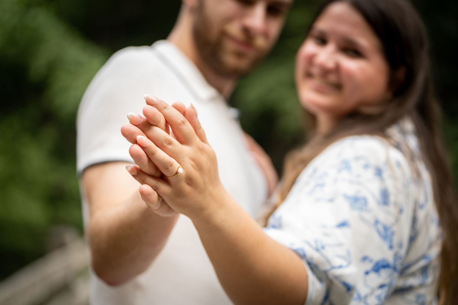 A close-up shot of hands clasped together during an emotional outdoor proposal moment.