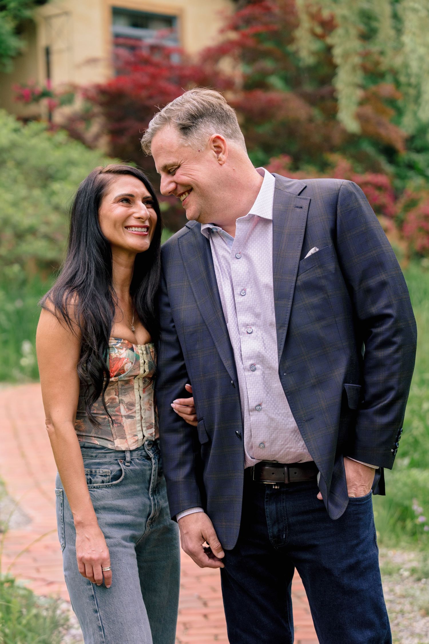 A romantic couple shares tender moments on a garden path surrounded by lush greenery and red foliage.