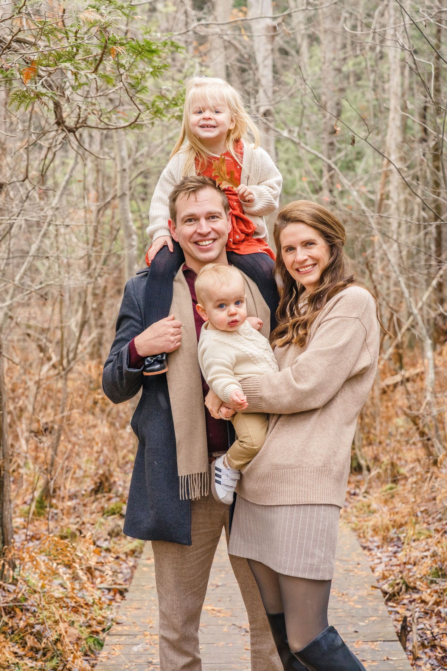 Family enjoying a playful autumn walk together on a wooded trail covered in fallen leaves.
