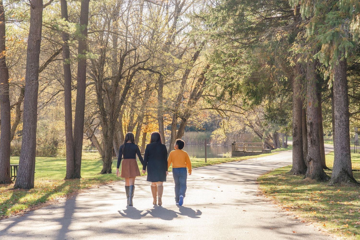 Two people walk together on a tree-lined path through a park on a sunny autumn afternoon.
