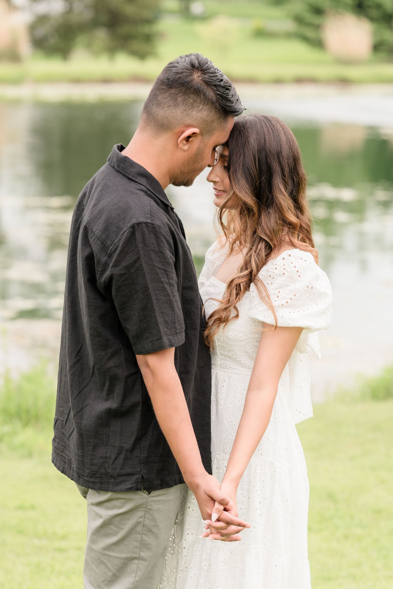 A couple shares an intimate moment on a lakeside lawn.
