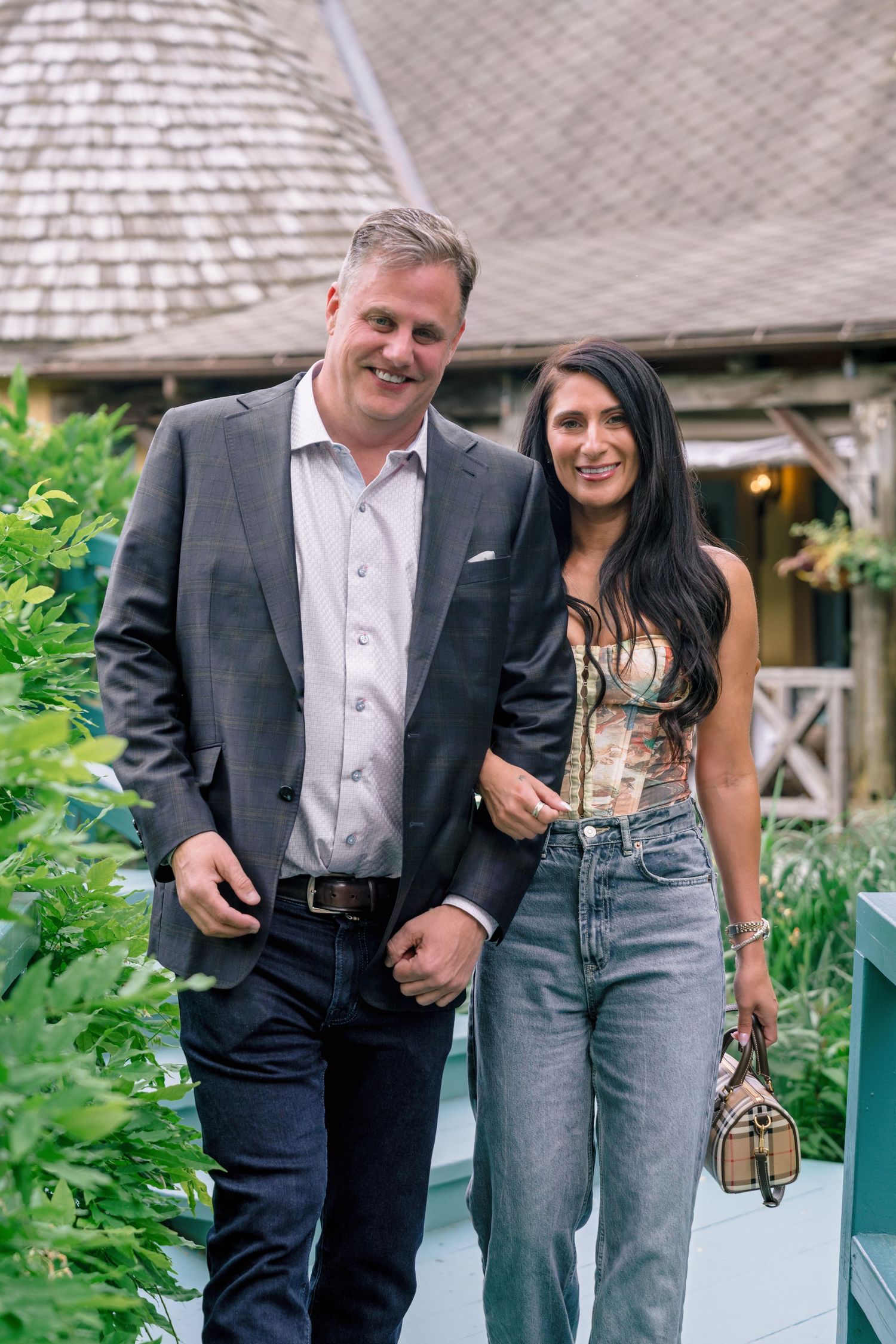 Couple laughing together on an outdoor patio with lush greenery in the background.