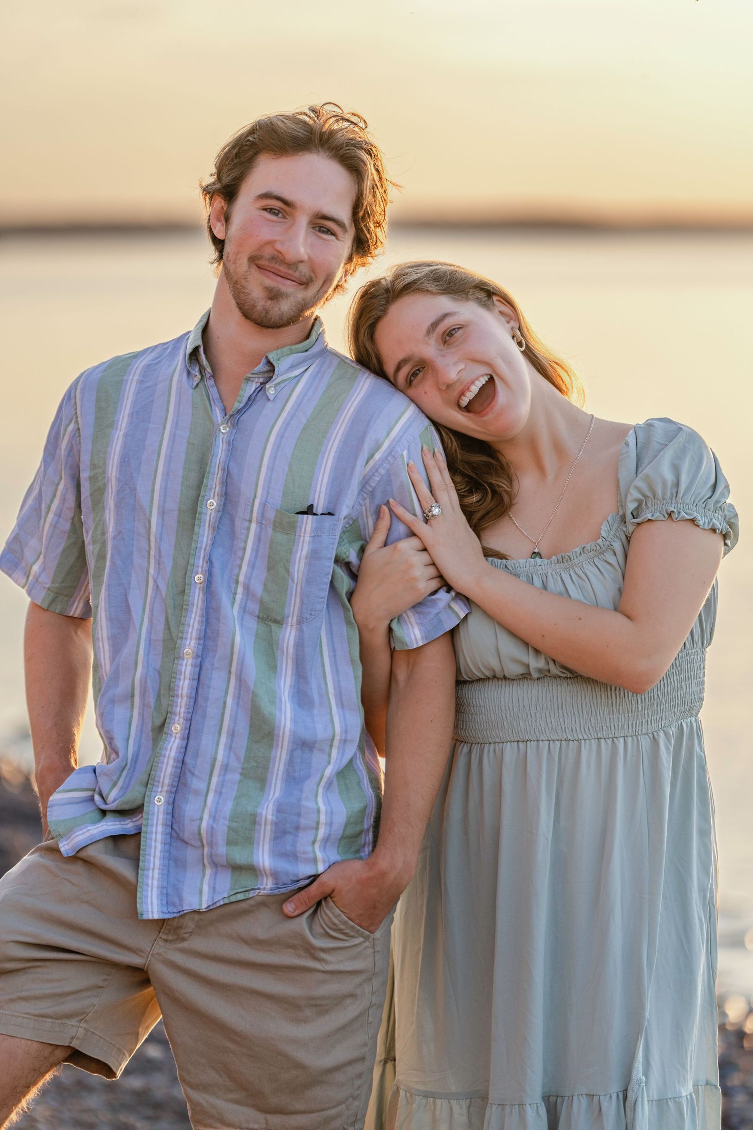 A joyful couple in coordinating outfits share a candid moment together at sunset by the water.