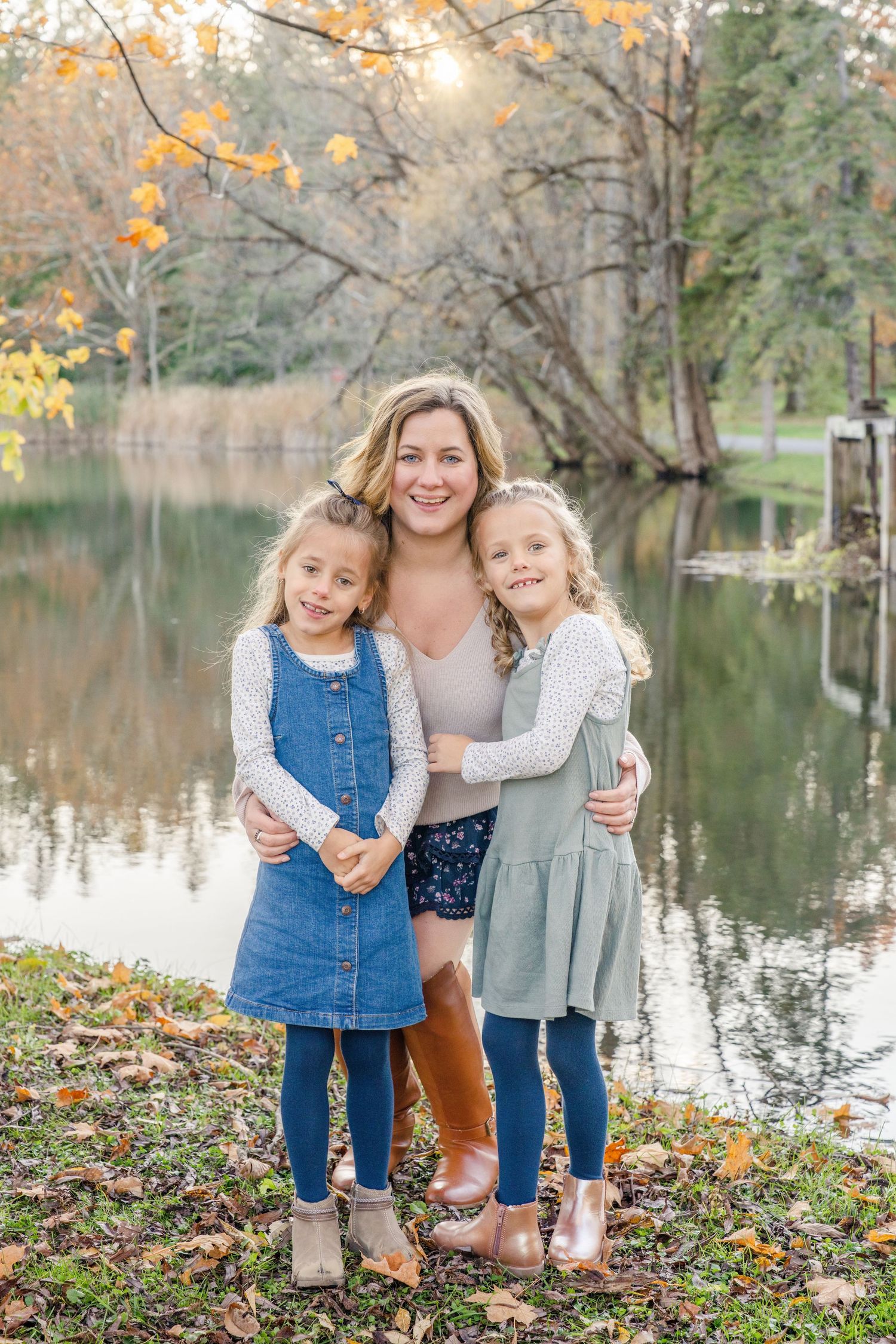 Family portrait session by a lake in autumn with fall foliage and reflective water in the background.