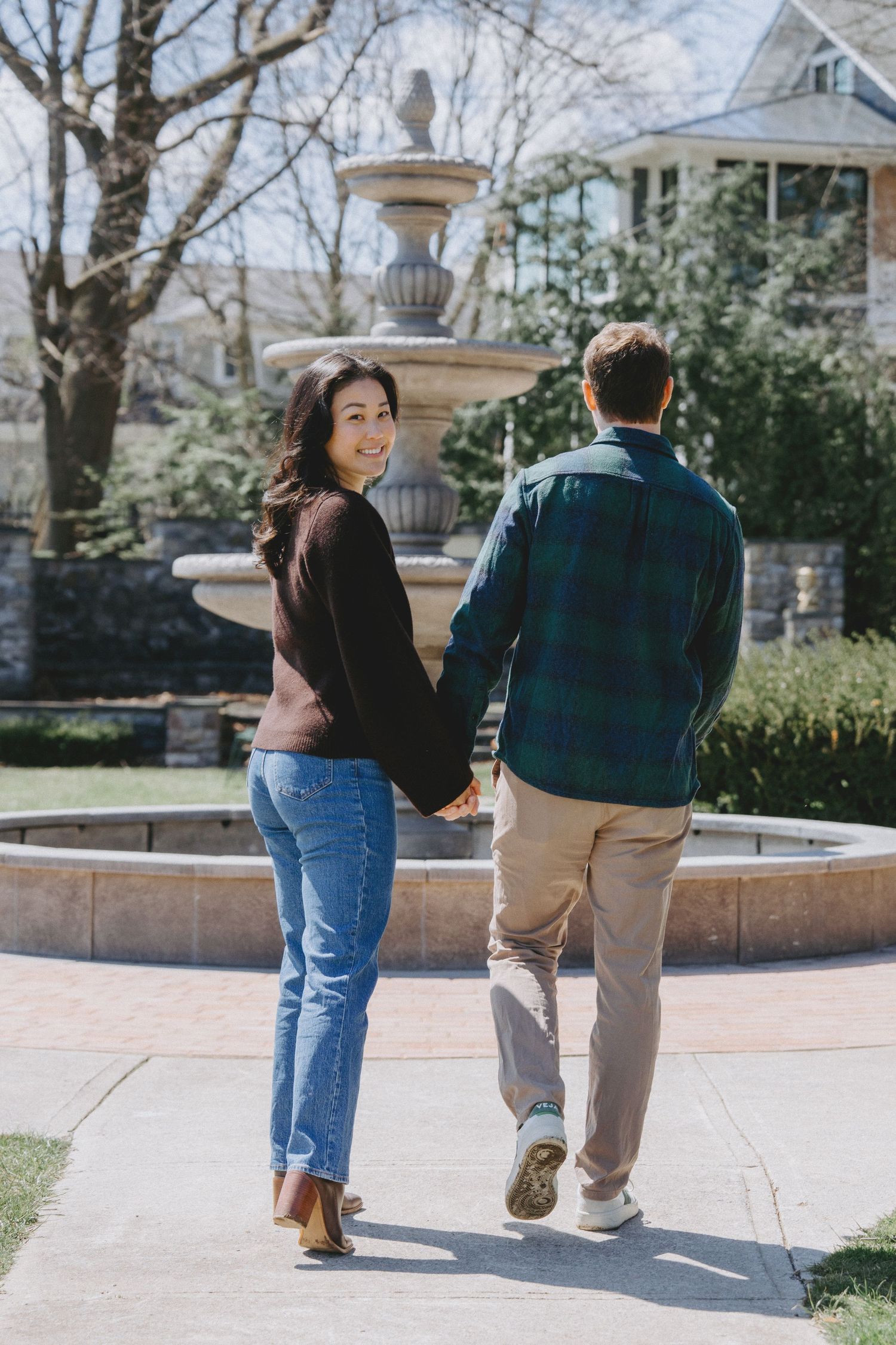 Two people walk together on a brick path through a sunny garden area on a spring day.