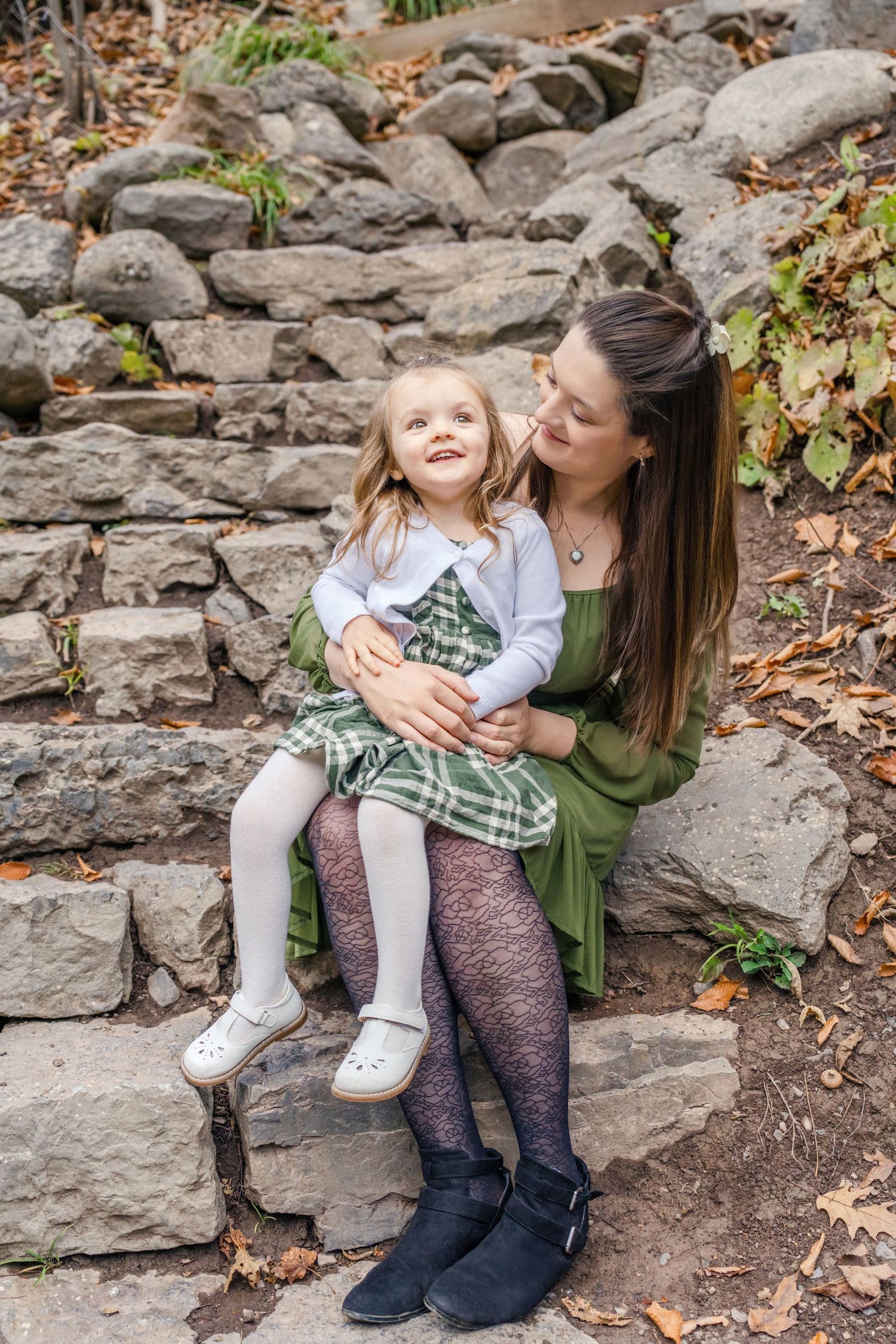 A parent and child share tender moments while sitting together on stone steps surrounded by fallen autumn leaves.